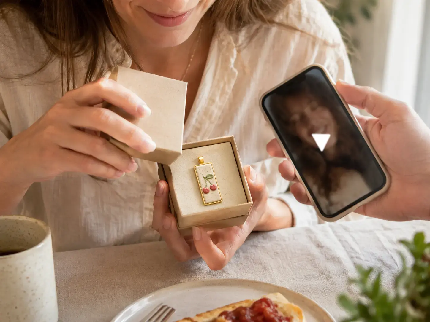 Recipient opening a ceramic HavenTap pendant gift beside a video message on a phone